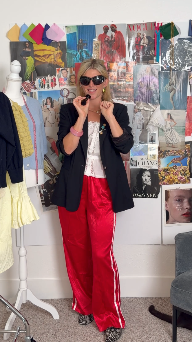 Sofie in a black blazer, white top, and red satin track pants, standing in her studio in front of a wall covered in fashion mood board clippings